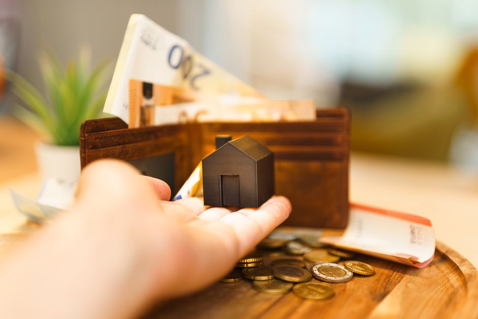 A close-up, professional photo of a person's hands separating a small stack of coins from a larger one next to a set of house keys, visually representing lower commission fees in a real estate sale.