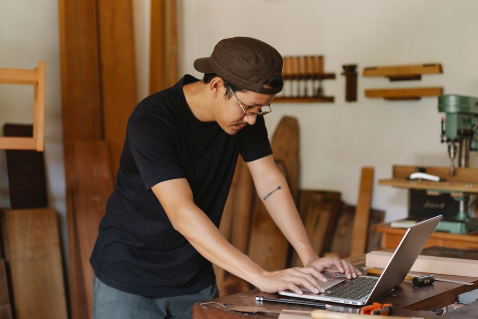 A home service business owner sits at a desk in a modern workshop, looking stressed while reviewing business performance on a laptop, highlighting the challenges of online marketing.