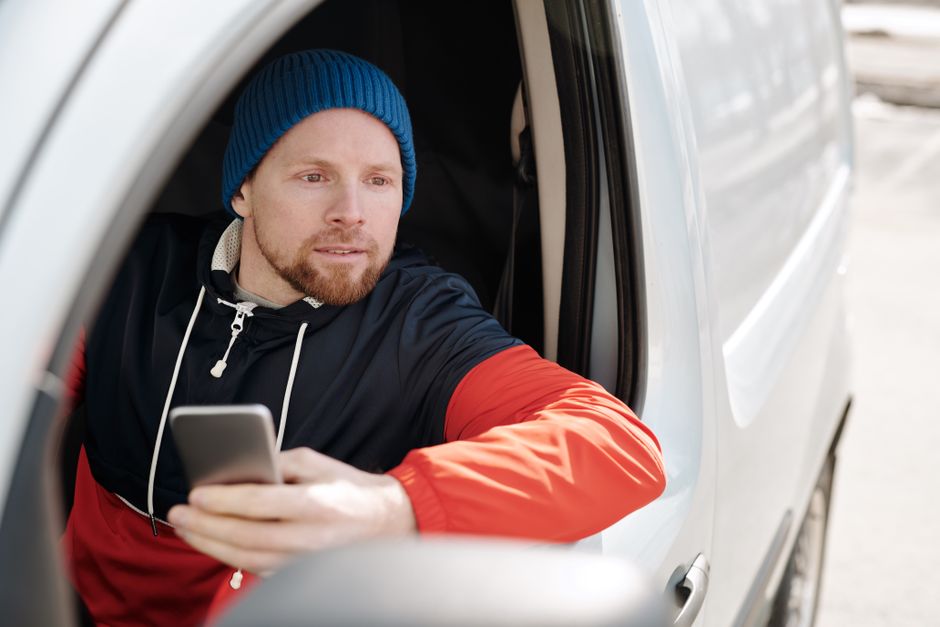 Professional home service contractor in a work van looks down at a silent smartphone with a concerned expression, symboliz...
